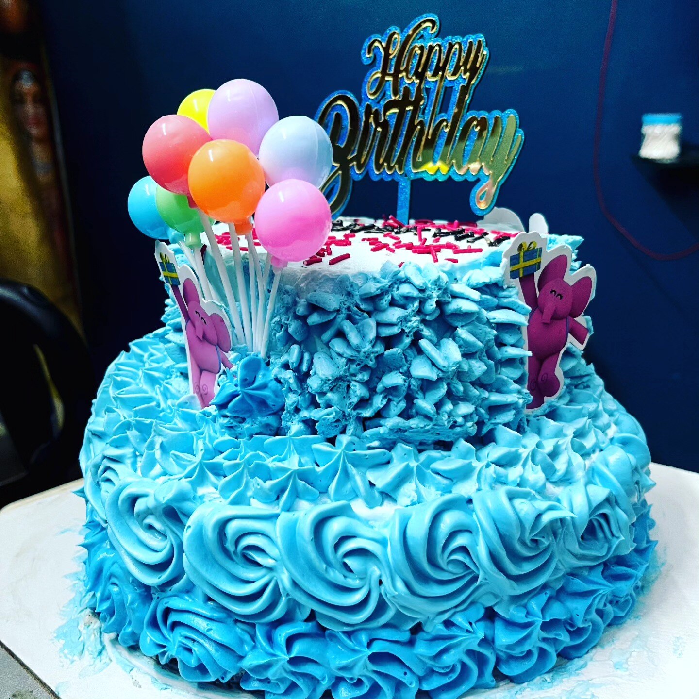 Blue rosette birthday cake with a Happy Birthday topper and balloons